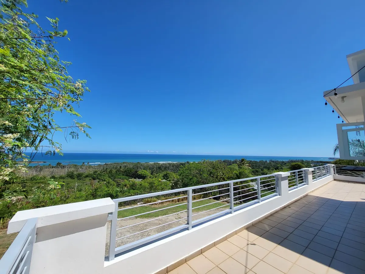 The white balcony railing, the green treeline and the deep blue sea in the morning