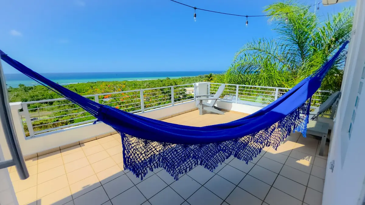 A blue hammock on the balcony, the sea and a palm behind it