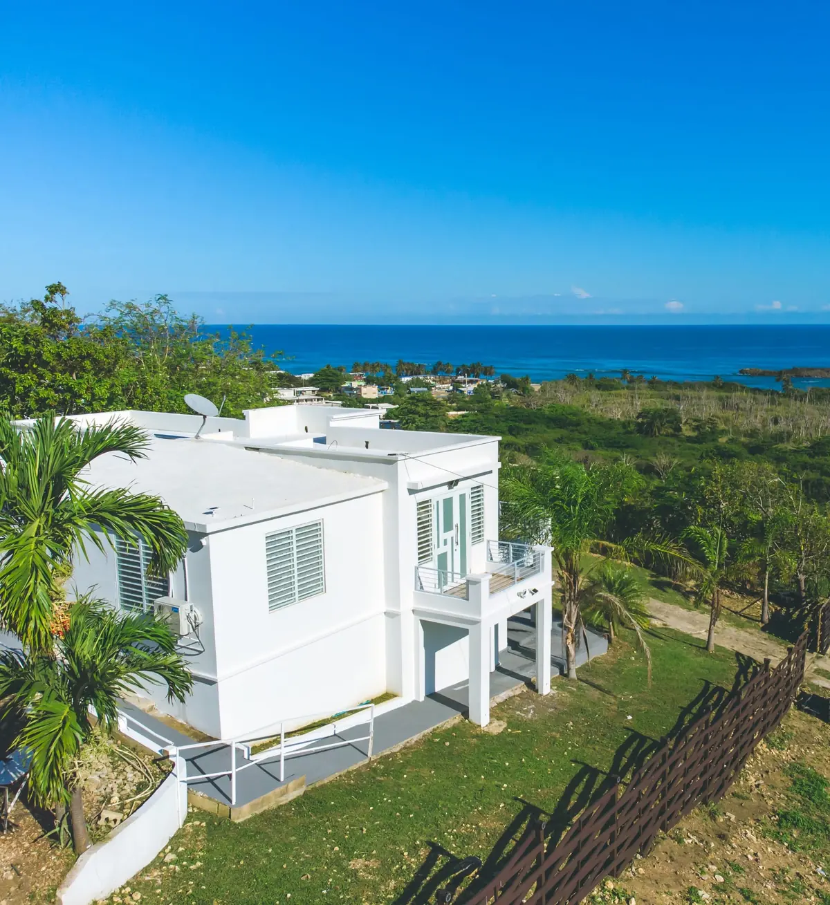 The white house from above, palm trees, the terrace and the sea behind