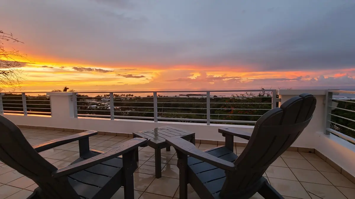 Two chairs on wet tiles at sunset, the sky orange and violet over the sea